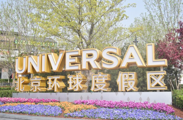 Gold Universal Beijing Resort entrance lettering rises above colourful flower beds, with leafy trees behind the bilingual sign.