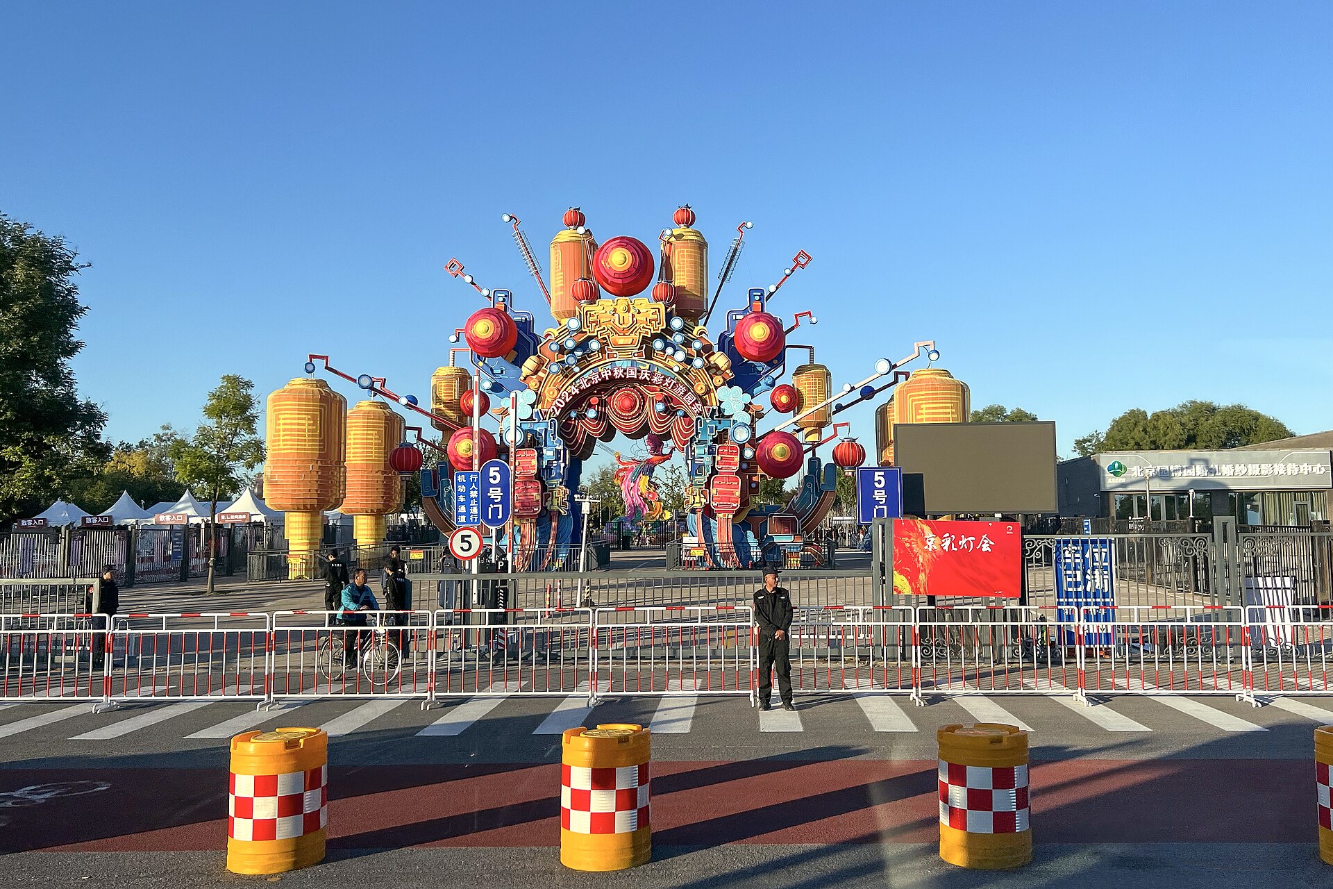 Golden lanterns decorate an elaborate festival arch at Gate 5 of Beijing Garden Expo Park under a clear sky.