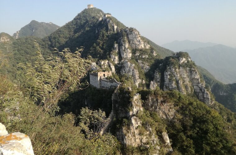The Great Wall at Jiankou clings to jagged rocky ridges, with ruined watchtowers scattered across wooded mountain peaks.