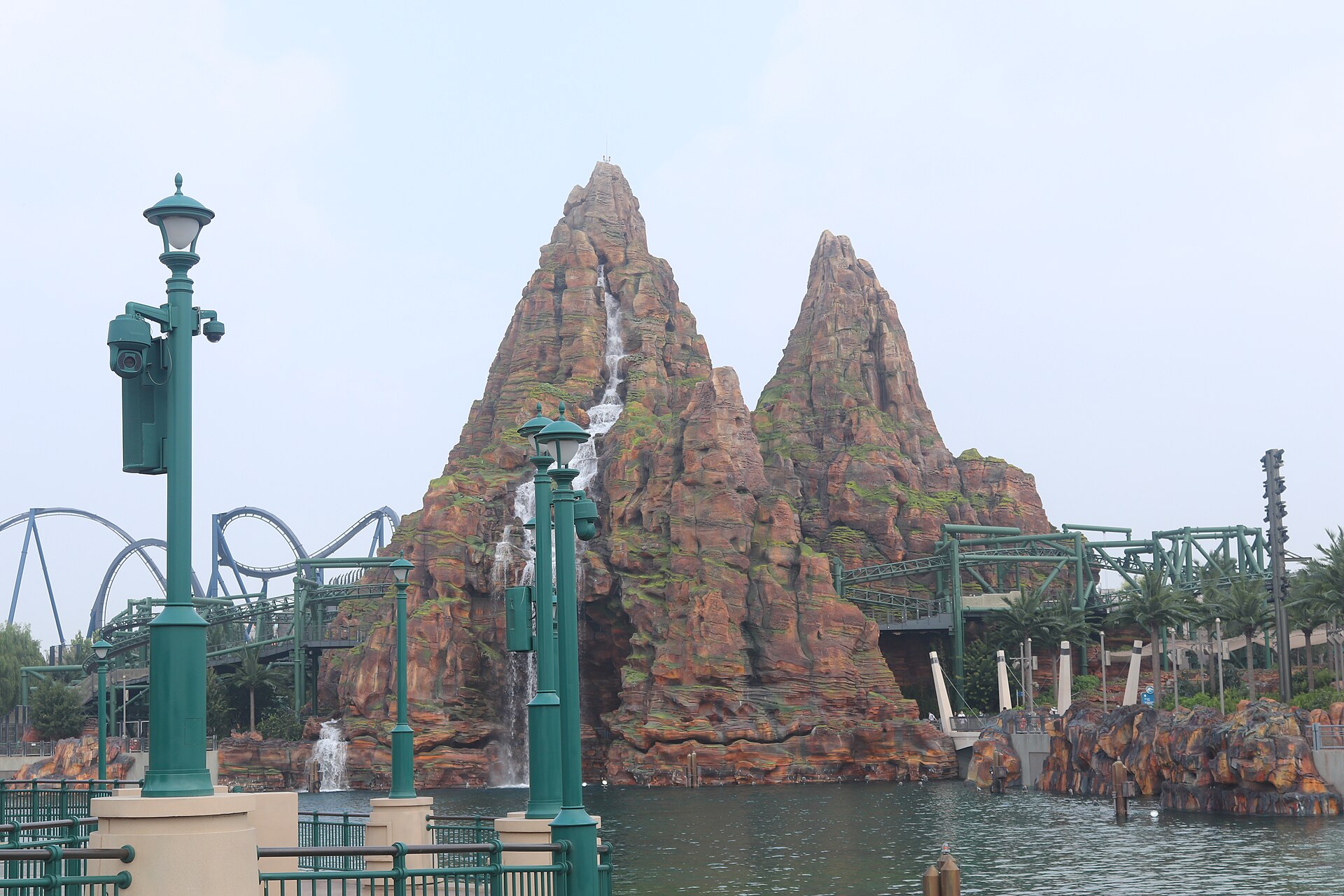 Green Jurassic Flyers track curves around rocky peaks and a waterfall above a lagoon at Universal Studios Beijing.