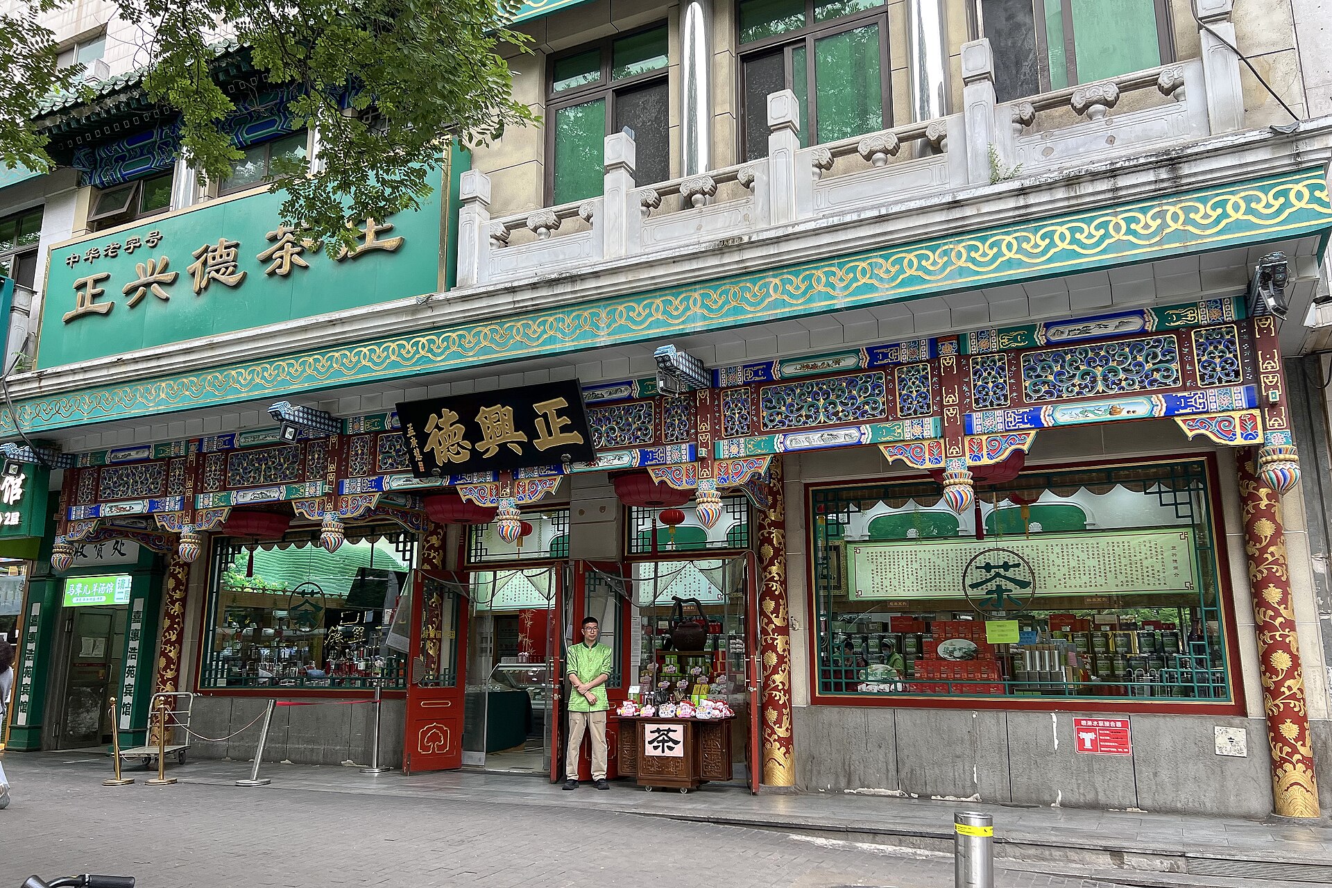 Green signs and ornate painted beams frame the Zheng Xing De tea shop on Beijing Niujie, with packaged tea visible inside.