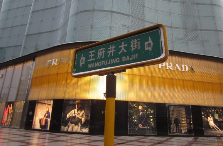 A green Wangfujing Dajie street sign in Beijing displays Chinese characters and romanized lettering above a tiled pavement.