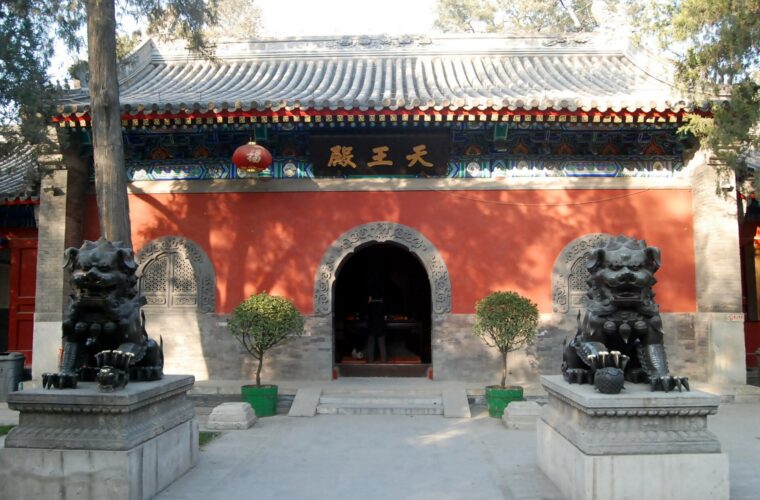 Guardian lions flank the arched doorway of Fayuan Temple's Hall of Heavenly Kings beneath painted eaves in Beijing.
