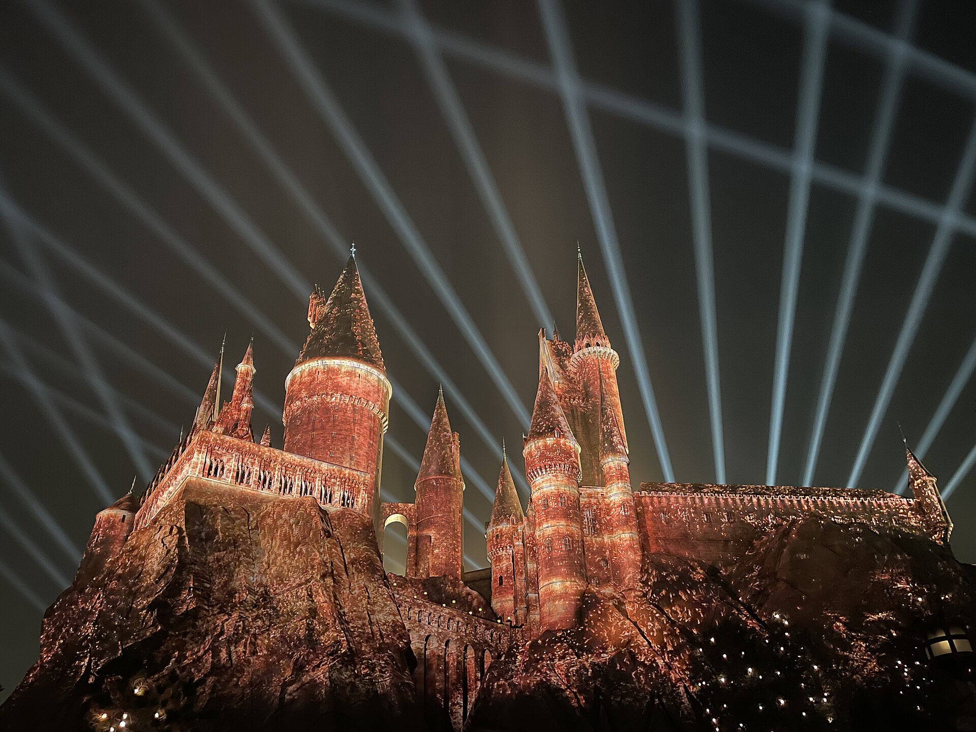 Hogwarts Castle at Universal Beijing Resort glows red and gold beneath white beams of light crossing the night sky.