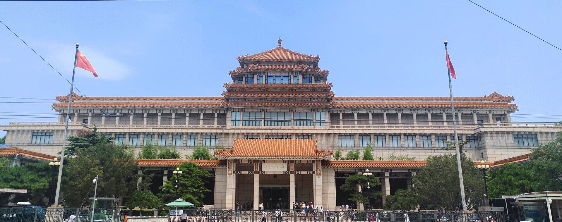 The National Art Museum of China on Wusi Street in Beijing, a large building with tiered orange-tiled roofs, flags on either side and visitors at the entrance