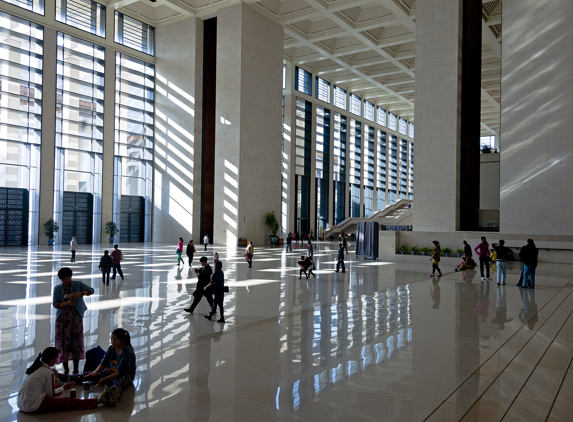 Visitors crossing the vast stone-floored front foyer of the National Museum of China, lit by tall windows that throw long bands of light across the floor