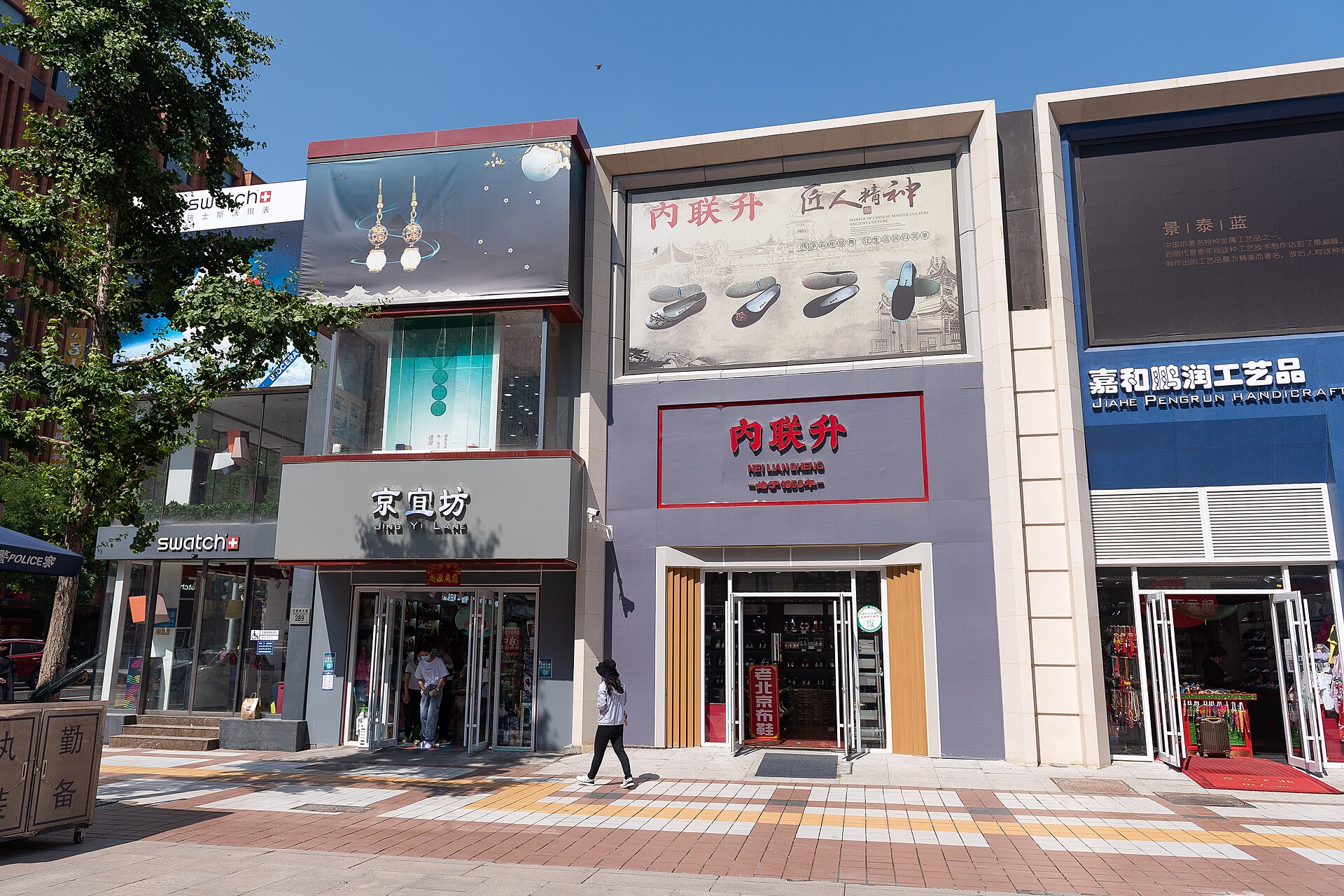 Neiliansheng shoe-shop signs and neighboring storefronts face the sunlit pedestrian pavement on Wangfujing Street in Beijing.