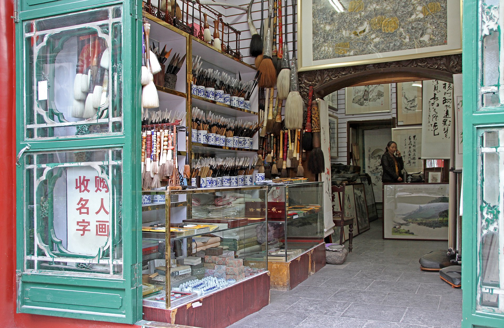 An open shop in Beijing Liulichang displays calligraphy brushes, framed paintings and scrolls behind green doors and a glass counter.