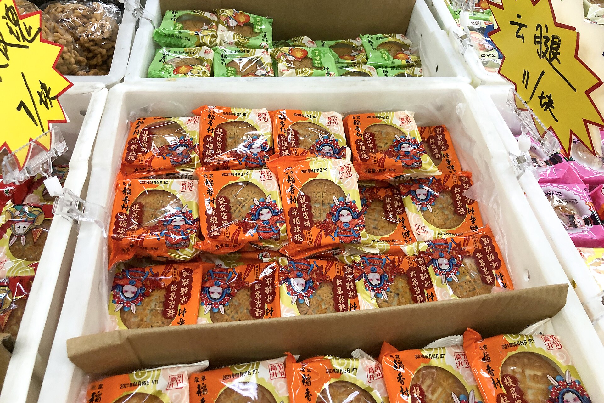 Orange-wrapped mooncakes fill a display bin beneath yellow price signs at Beijing Daoxiangcun in Xibeiwang, with green packages behind.