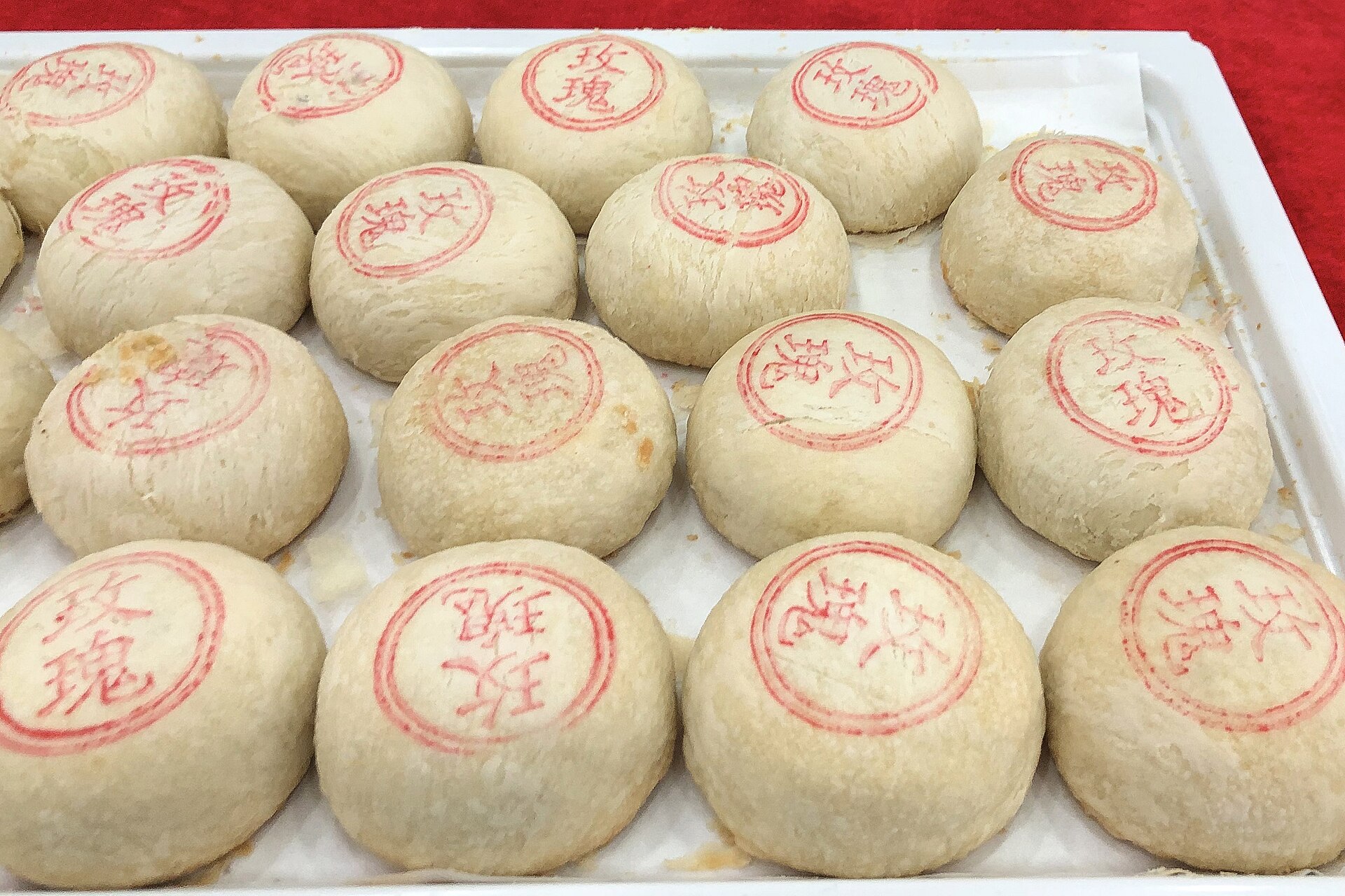 Pale rose-filled mooncakes with red stamped characters sit in rows on a white tray at Beijing Daoxiangcun.