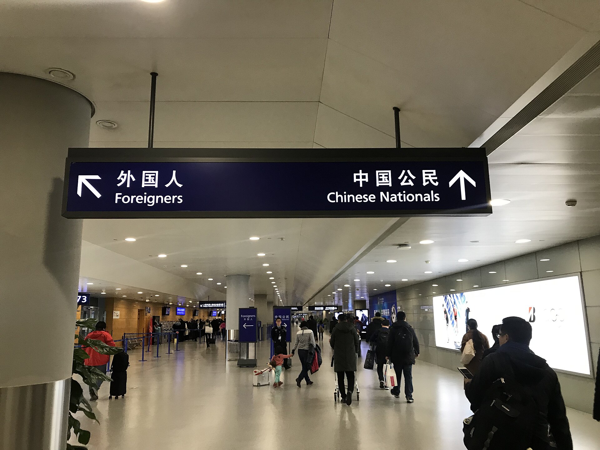 Passengers carrying luggage follow Chinese and English immigration signs for foreigners and Chinese nationals inside Shanghai Pudong International Airport.