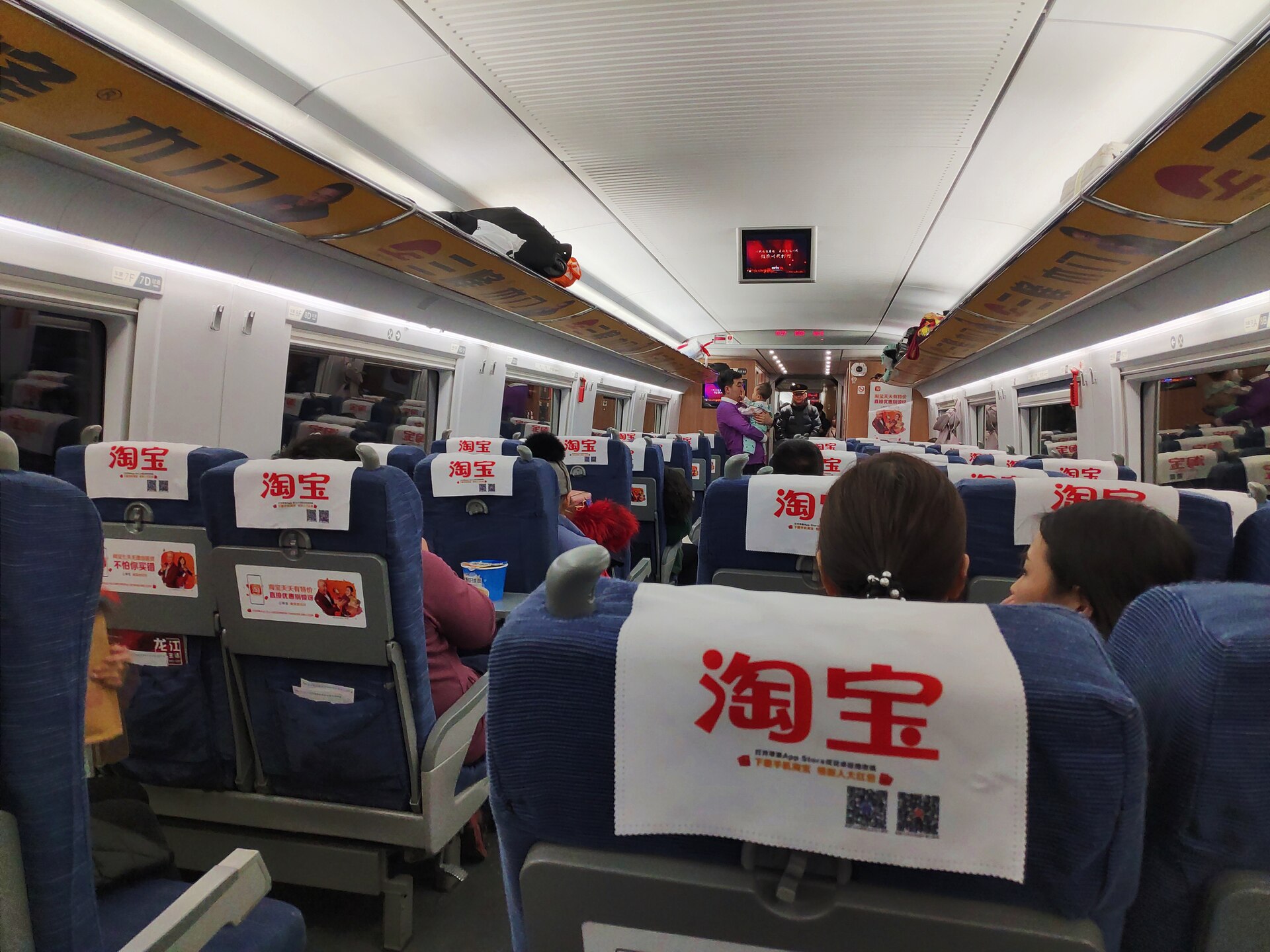 Passengers occupy blue second-class seats in a three-plus-two layout inside a Chinese CRH train, with bags on overhead racks.