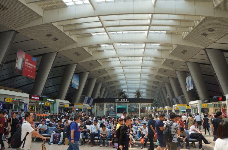 Passengers sit and stand with luggage beneath the high skylit roof and numbered boarding gates at Beijing South Railway Station.