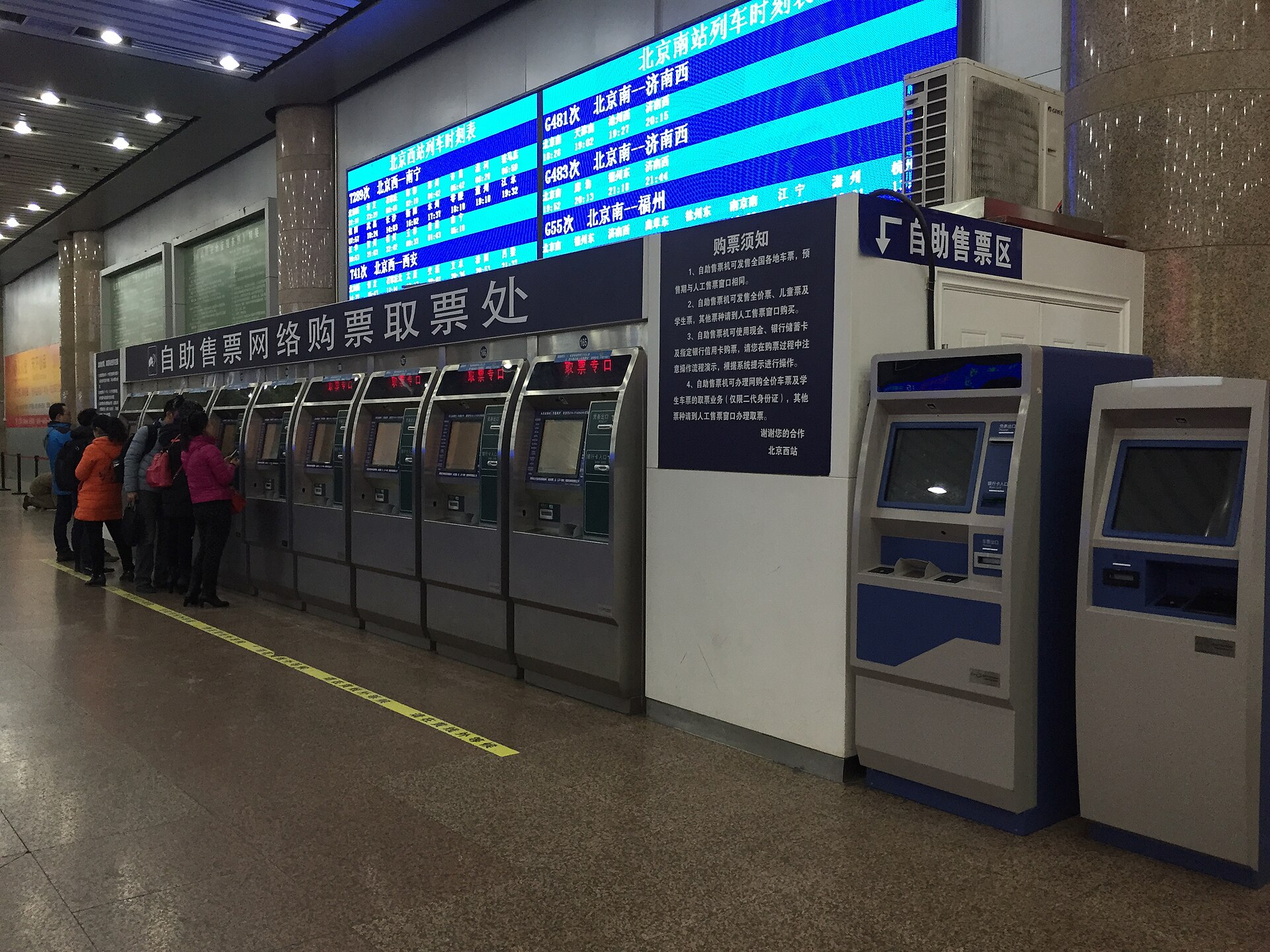 Passengers use railway ticket machines in Beijing beneath signs for self-service sales and collection of tickets purchased online.