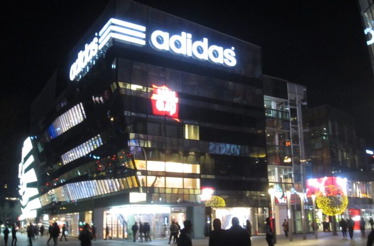 Pedestrians cross the illuminated plaza beside the Adidas storefront at Taikoo Li Sanlitun in Beijing at night.