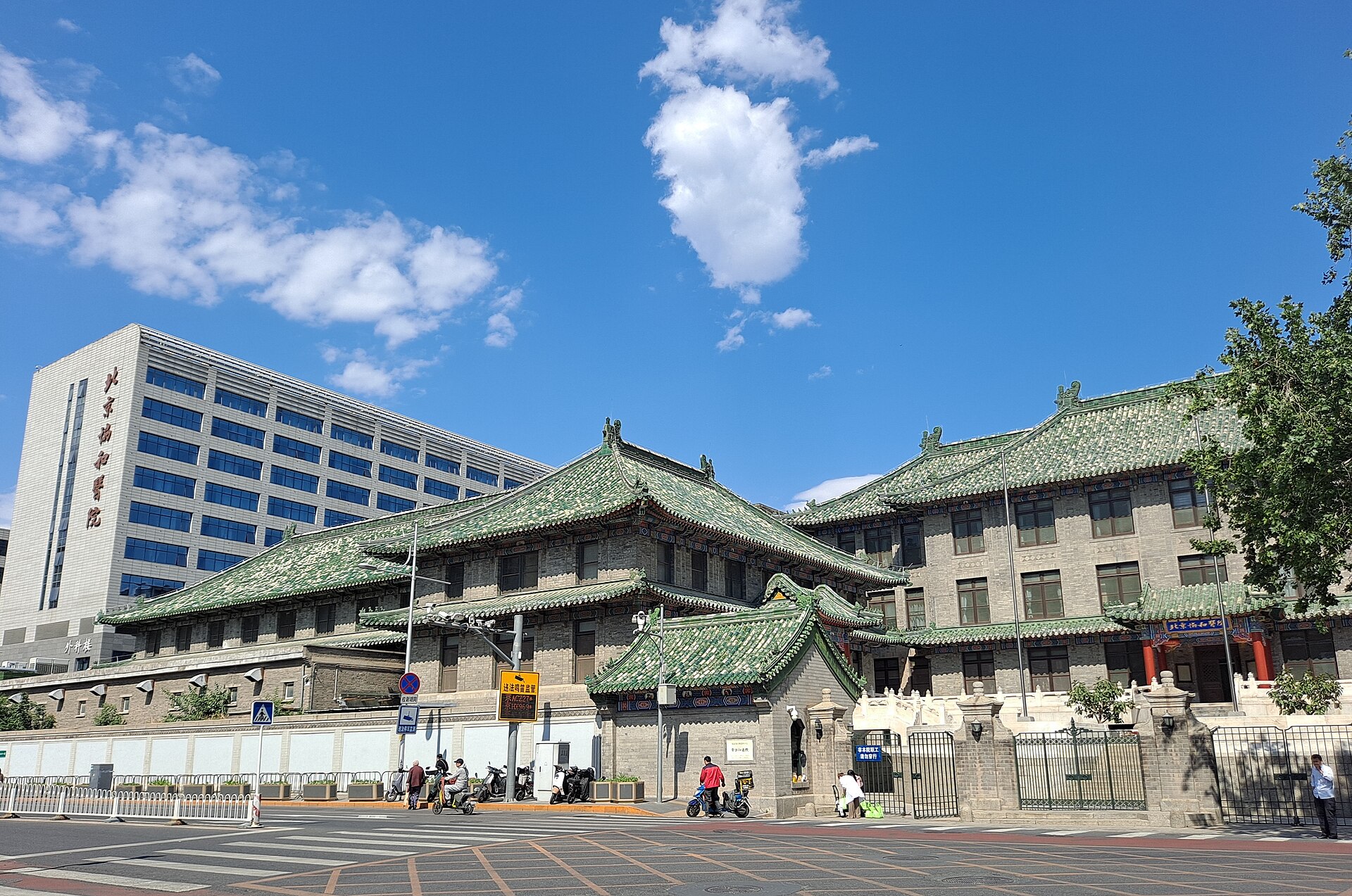 Peking Union Medical College Hospital in Beijing has green-tiled roofs beside a taller modern building, with pedestrians along the street.
