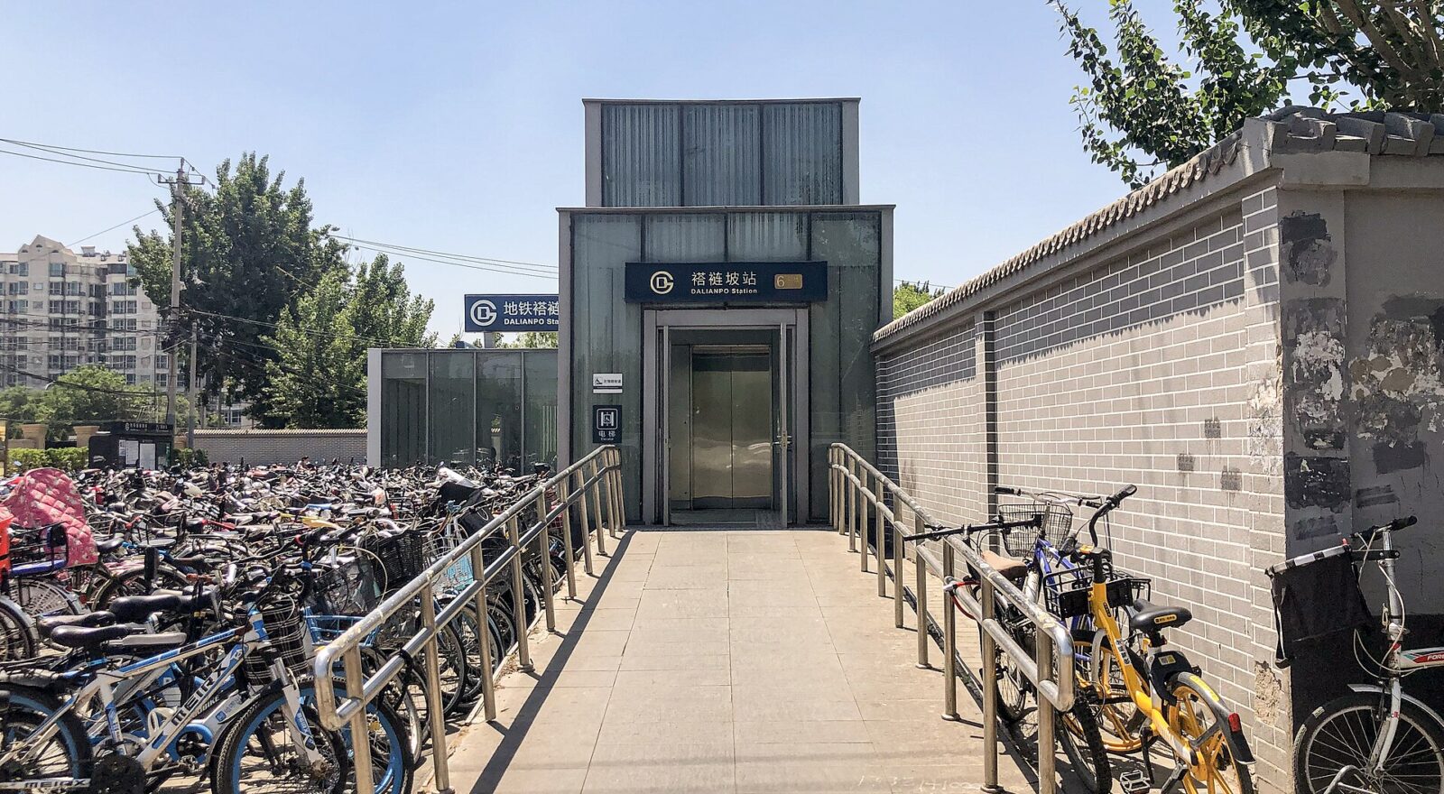 A ramp with metal handrails leads to the lift at Dalianpo subway station in Beijing, beside rows of parked bicycles.