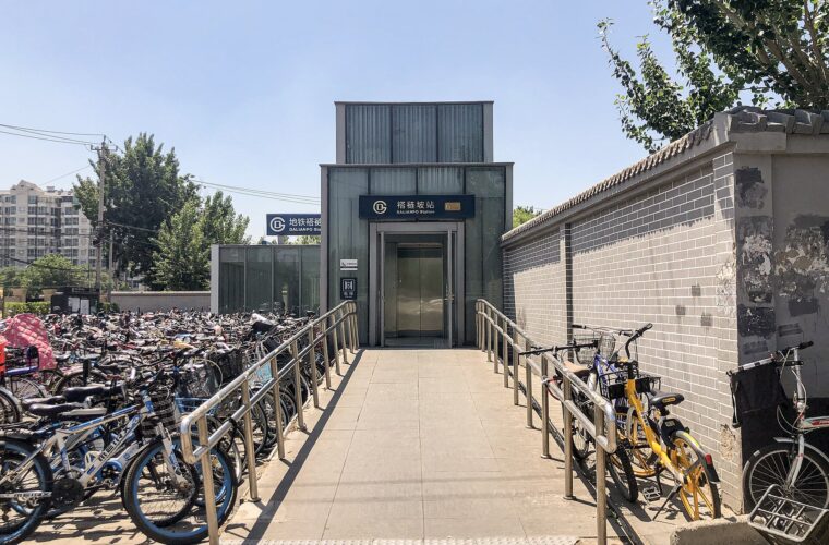 A ramp with metal handrails leads to the lift at Dalianpo subway station in Beijing, beside rows of parked bicycles.