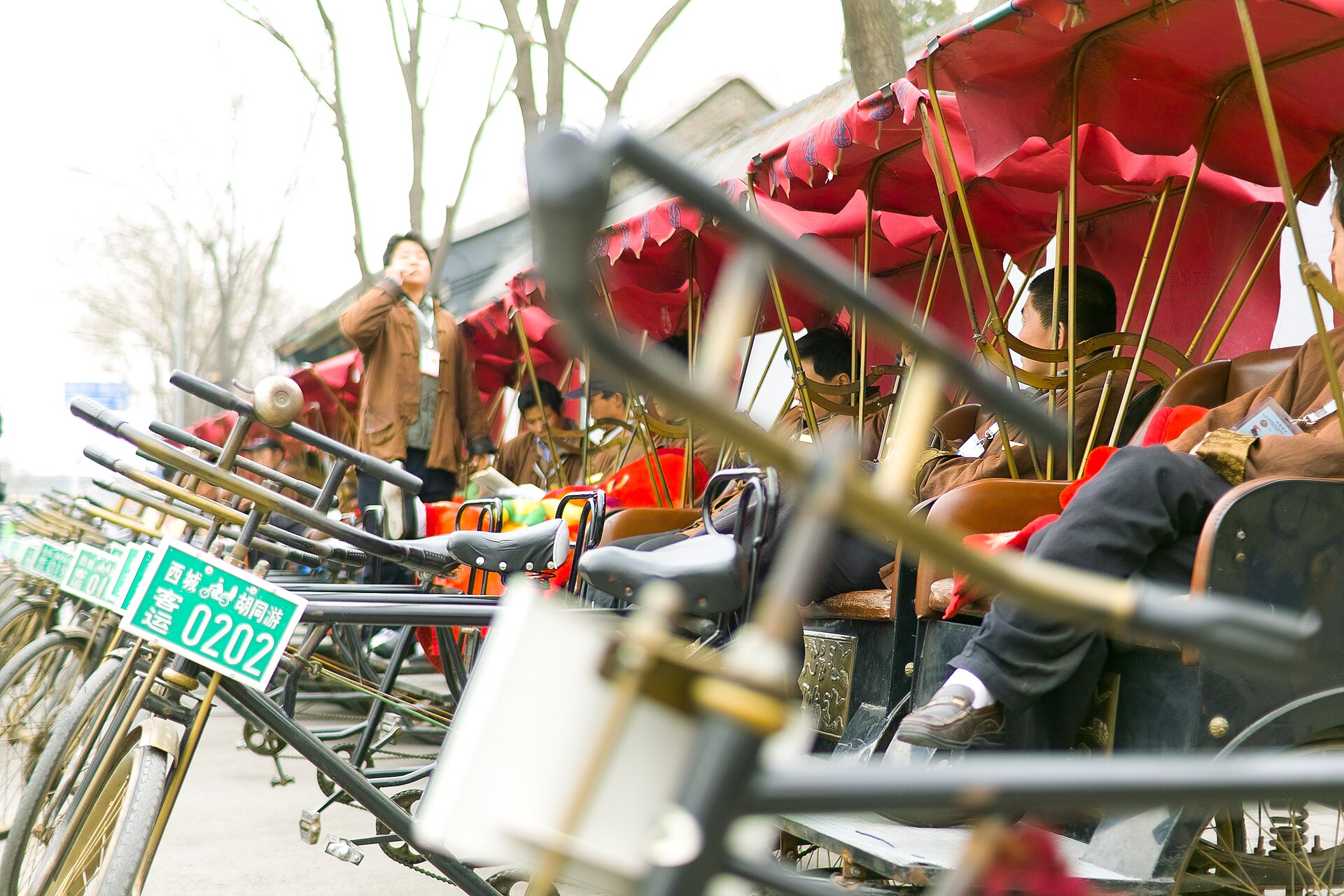 Red-canopied hutong tour rickshaws wait in a row at Shichahai, with green numbered plates mounted above their front wheels.