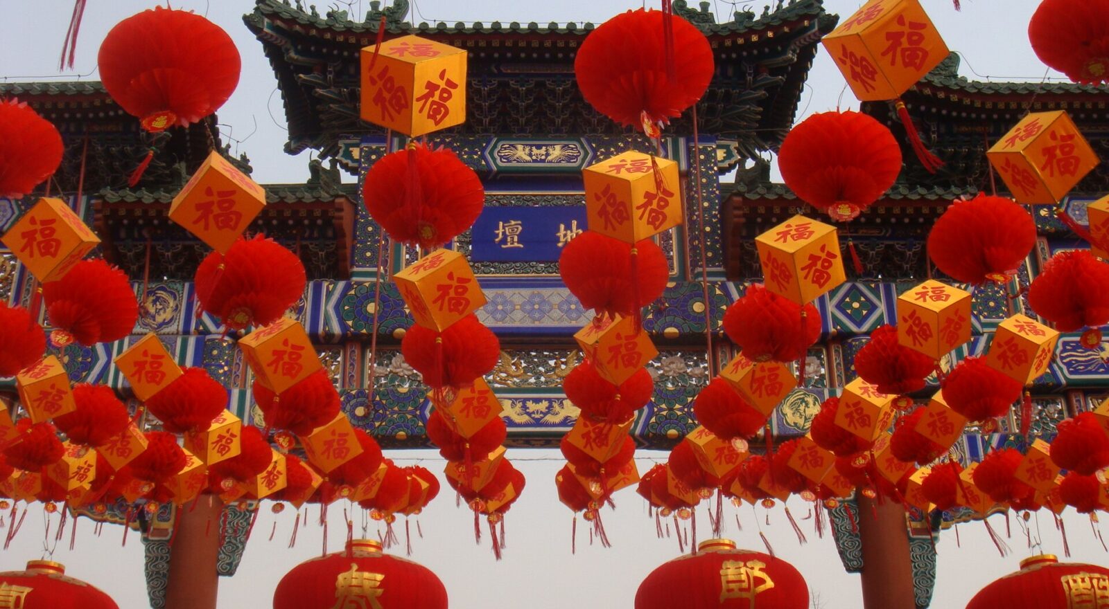Red lanterns and yellow blessing decorations hang before the ornate Ditan entrance arch during a Beijing temple fair.