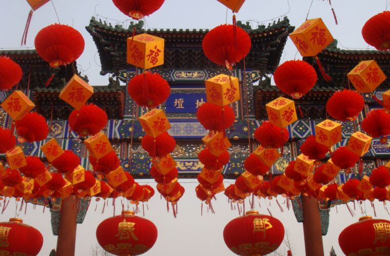 Red lanterns and yellow blessing decorations hang before the ornate Ditan entrance arch during a Beijing temple fair.
