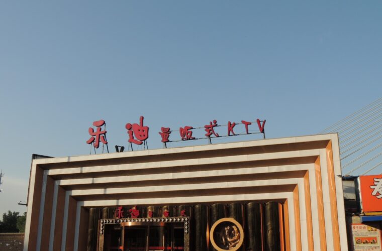 Red Ledi KTV lettering tops a striped karaoke venue entrance in Beijing Shangdi, with pedestrians and a parked red car.