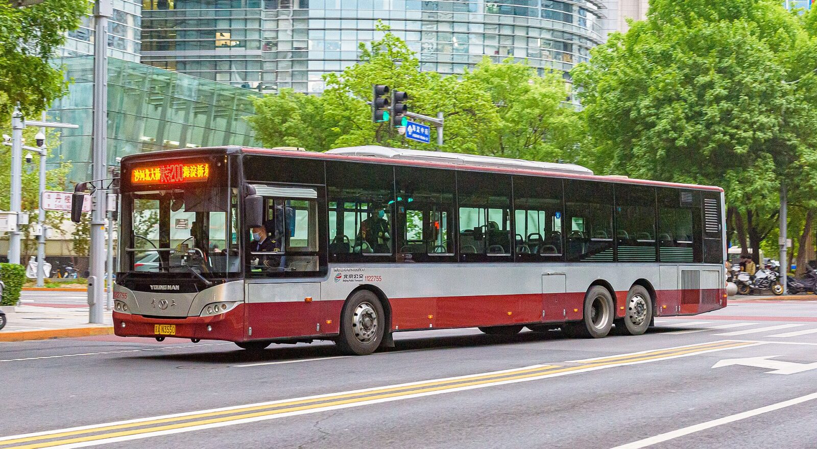 A red and silver Beijing public bus turns through a Zhongguancun junction beside glass office buildings and leafy trees.