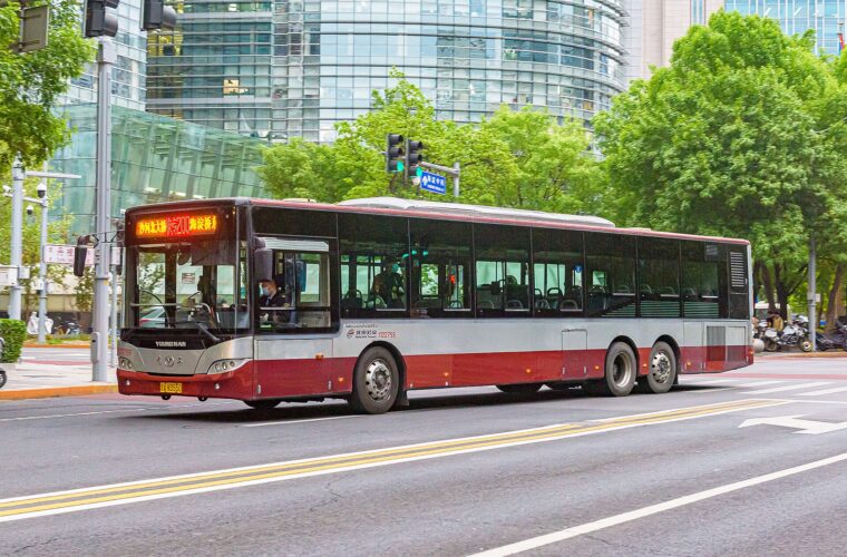 A red and silver Beijing public bus turns through a Zhongguancun junction beside glass office buildings and leafy trees.