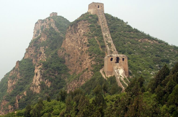 Ruined watchtowers at Gubeikou crown steep rocky ridges, linked by broken walls above densely vegetated slopes.