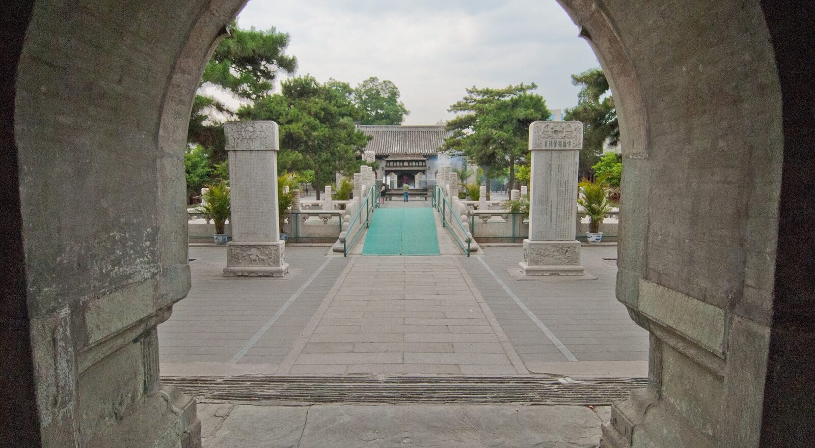 A stone arch frames paired stelae, a bridge and a grey-roofed hall in the courtyard of Beijing's White Cloud Temple.