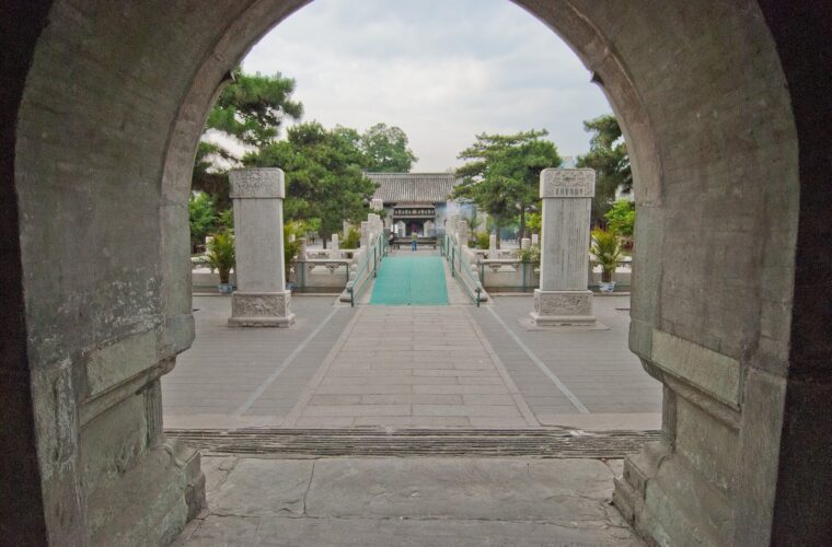 A stone arch frames paired stelae, a bridge and a grey-roofed hall in the courtyard of Beijing's White Cloud Temple.