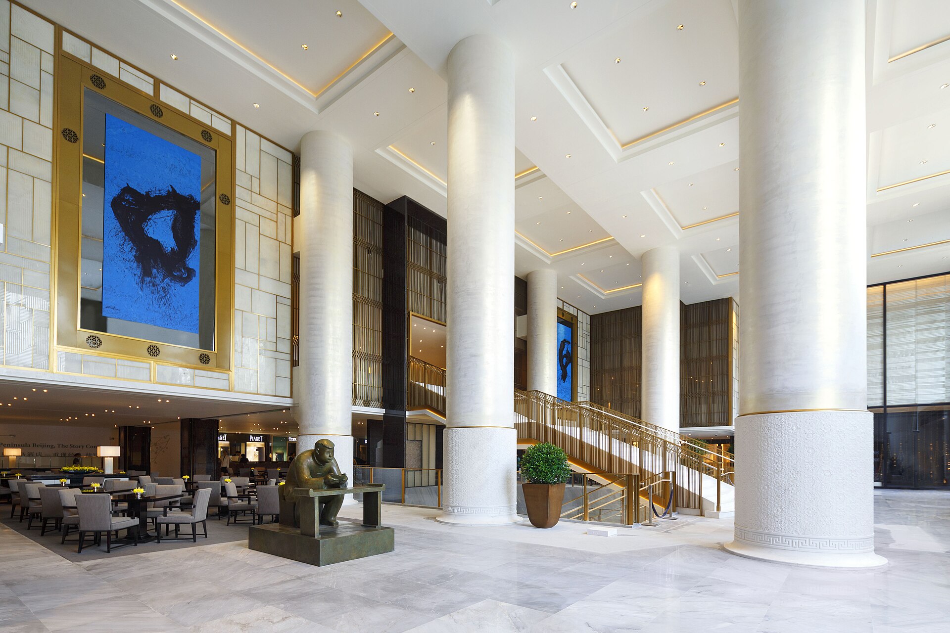 Tall white columns, blue paintings and a bronze sculpture surround the seating and staircase in The Peninsula Beijing lobby.