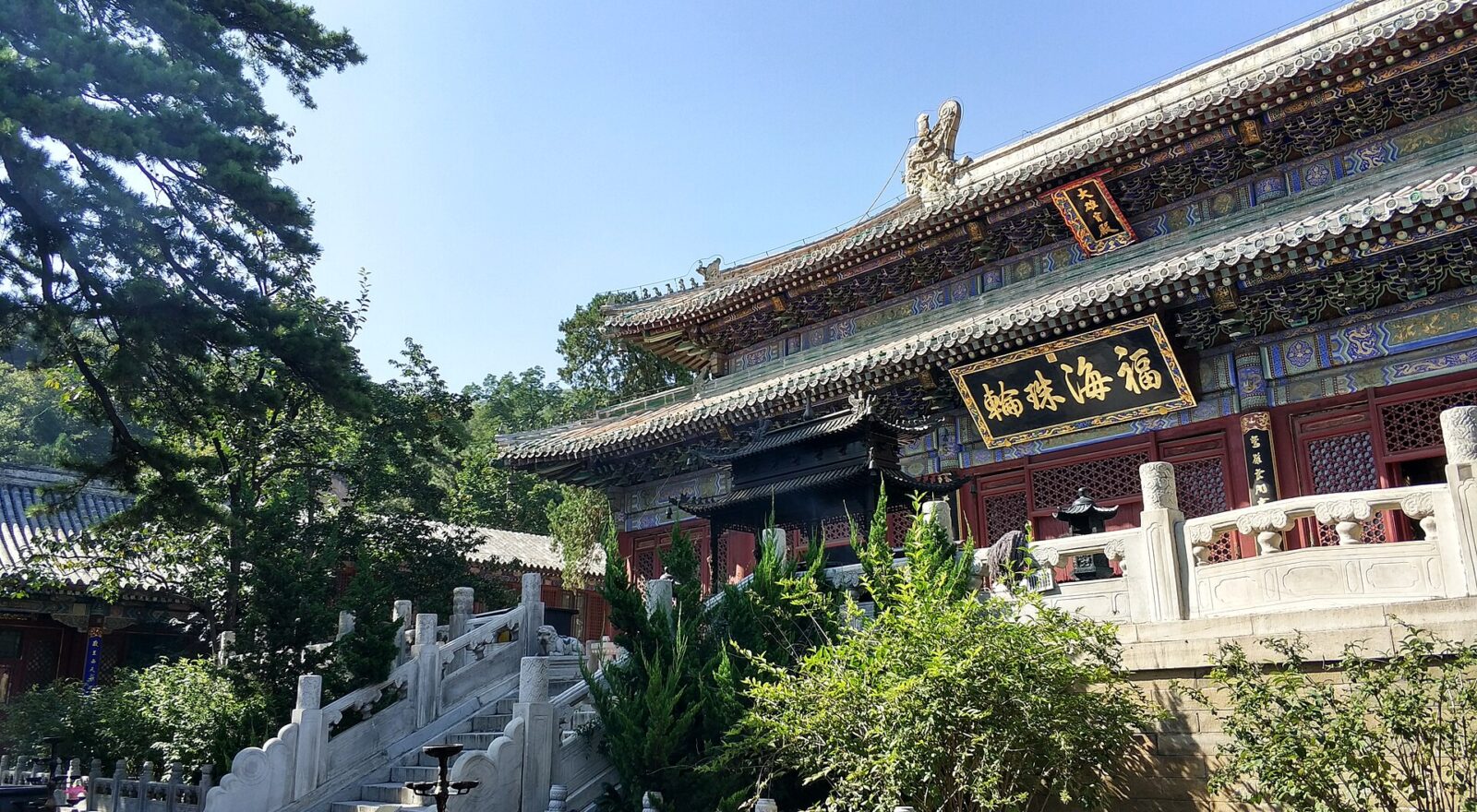 Tanzhe Temple in Beijing, with painted hall eaves, white stone stairways and green trees beneath a blue sky.