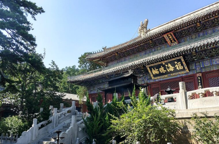 Tanzhe Temple in Beijing, with painted hall eaves, white stone stairways and green trees beneath a blue sky.
