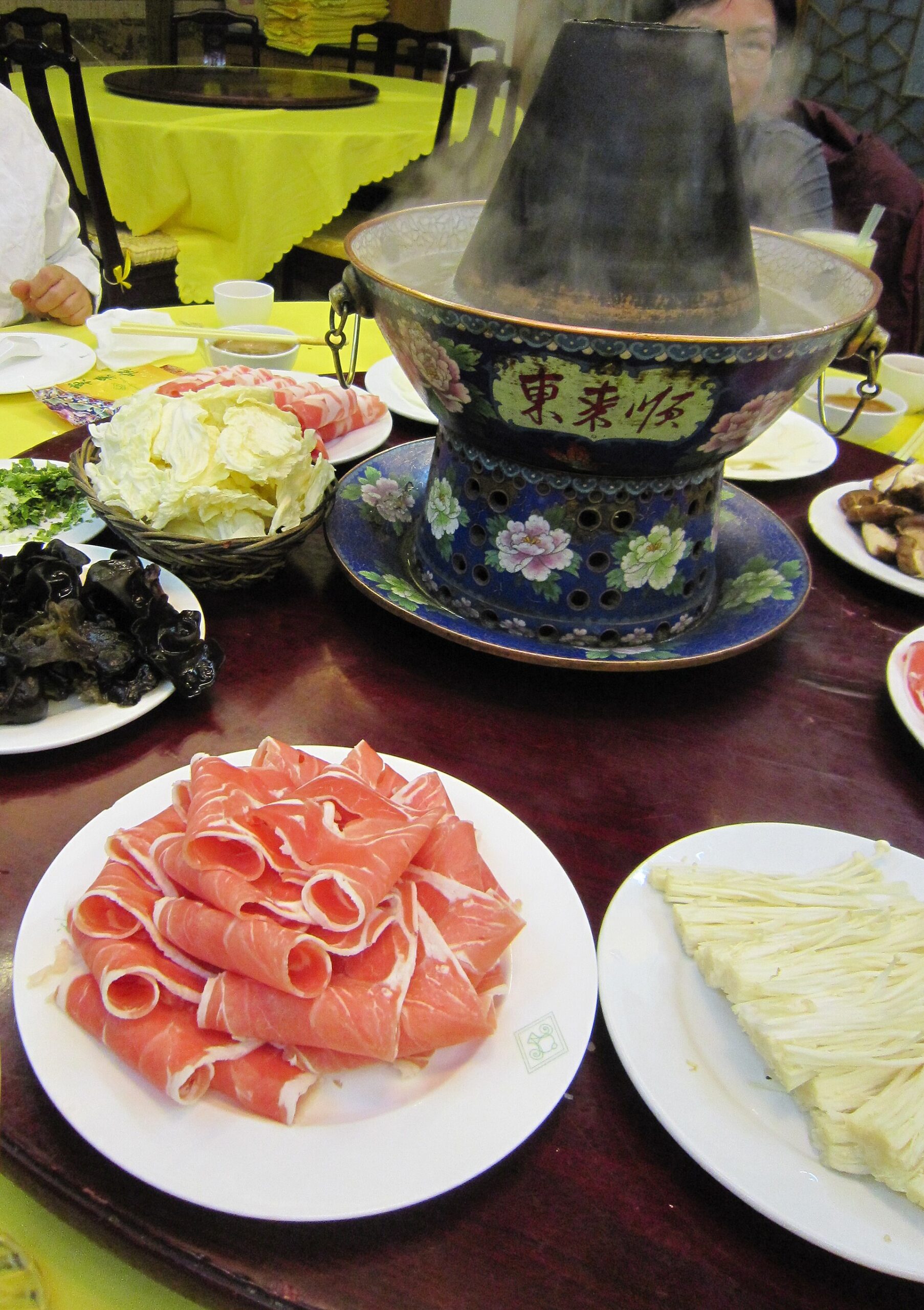 Thin lamb rolls and vegetables surround an enamelled chimney hot pot bearing Donglaishun's name at its Wangfujing restaurant in Beijing.