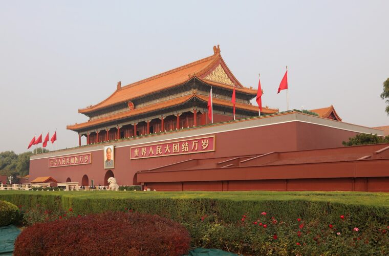 Tiananmen rises above clipped hedges in Beijing, with golden roofs, red flags and small groups of visitors along its base.