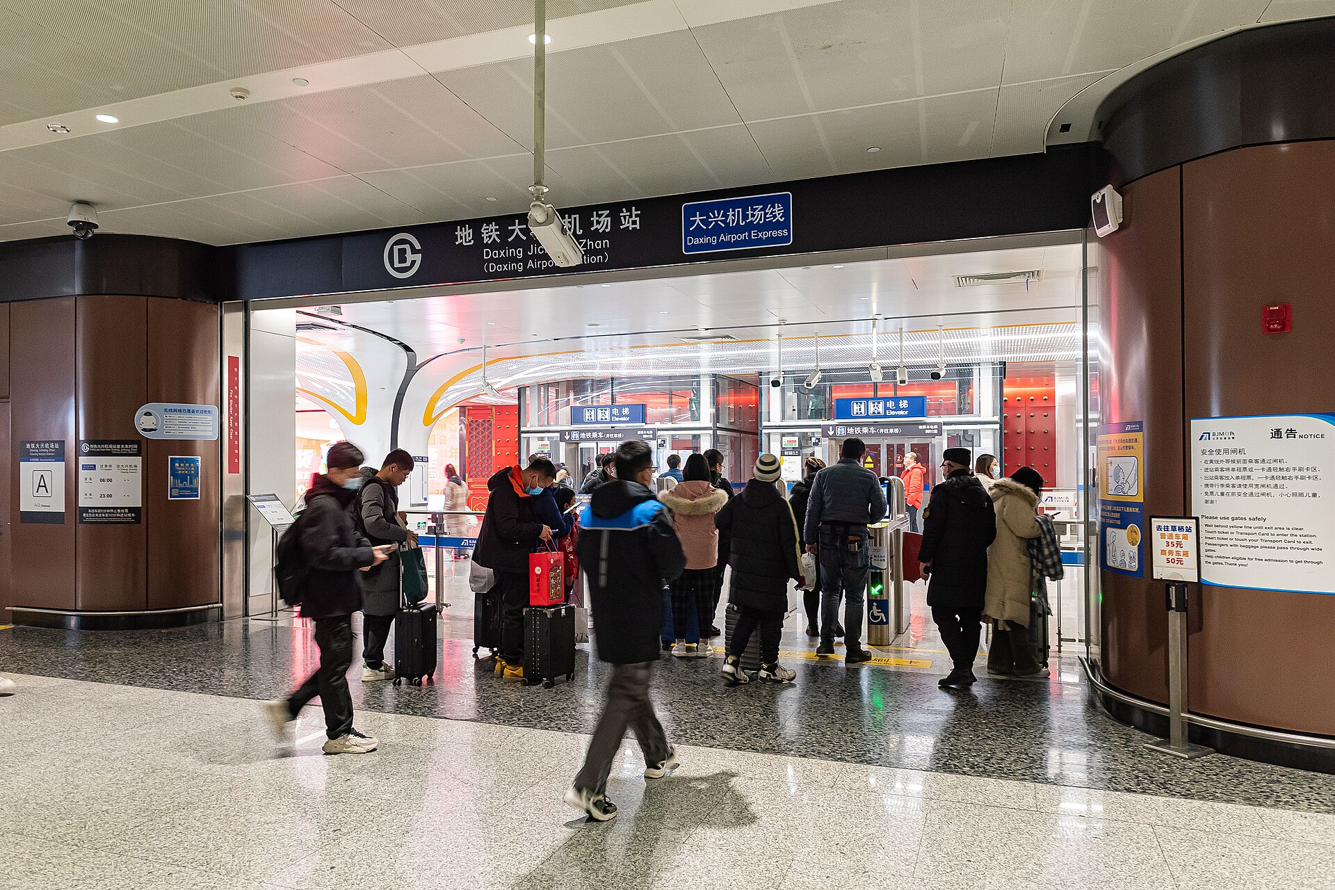 Travelers with luggage enter Beijing Daxing Airport Express station beneath bilingual signs above the fare gates.