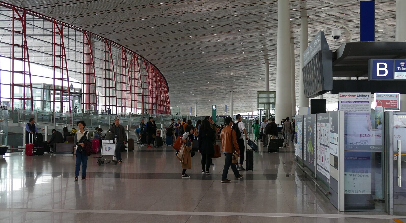 Travellers walk past airline counters beneath the sweeping ceiling and red window frames of Beijing Capital Airport Terminal 3.