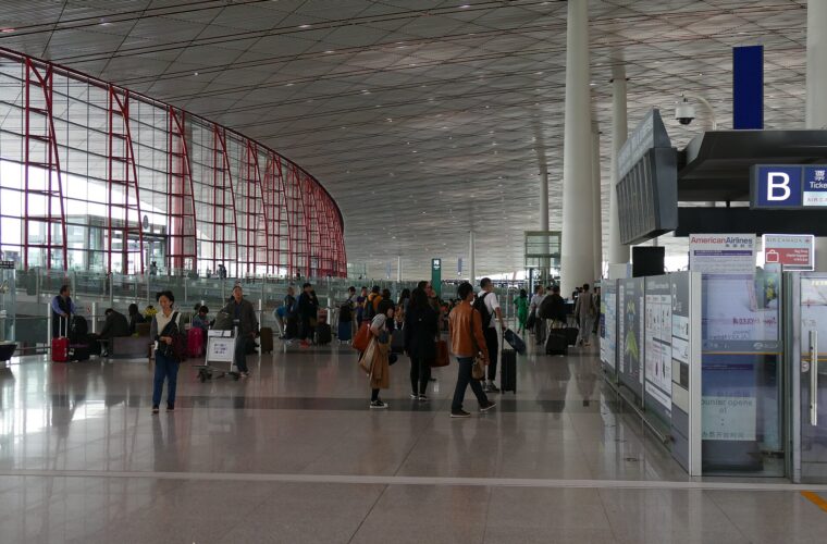 Travellers walk past airline counters beneath the sweeping ceiling and red window frames of Beijing Capital Airport Terminal 3.