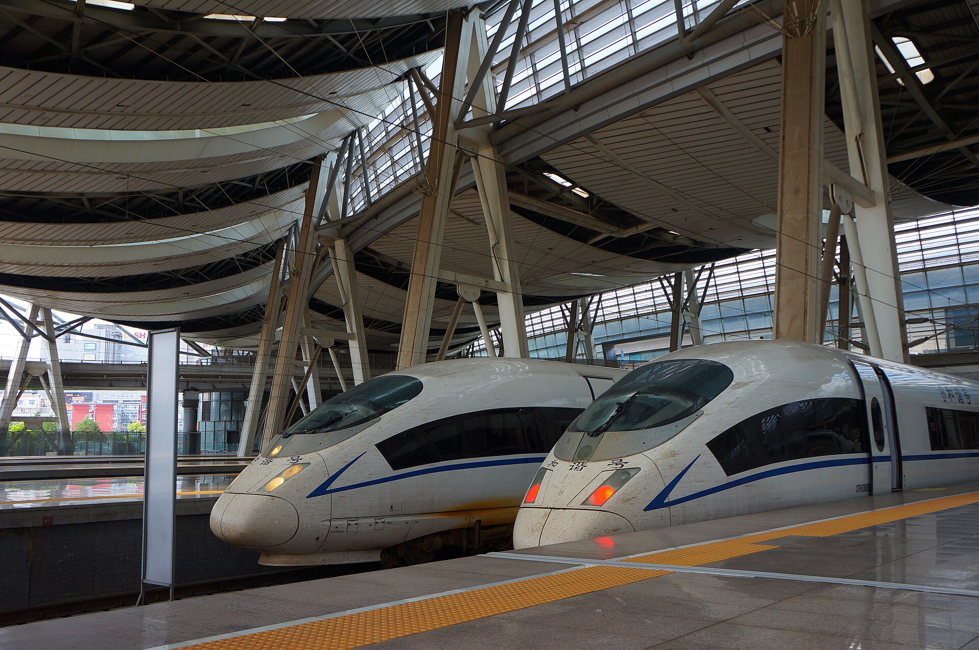 Two white CRH high-speed trains stand beside a yellow-edged platform under the tall canopy at Beijing South Railway Station.