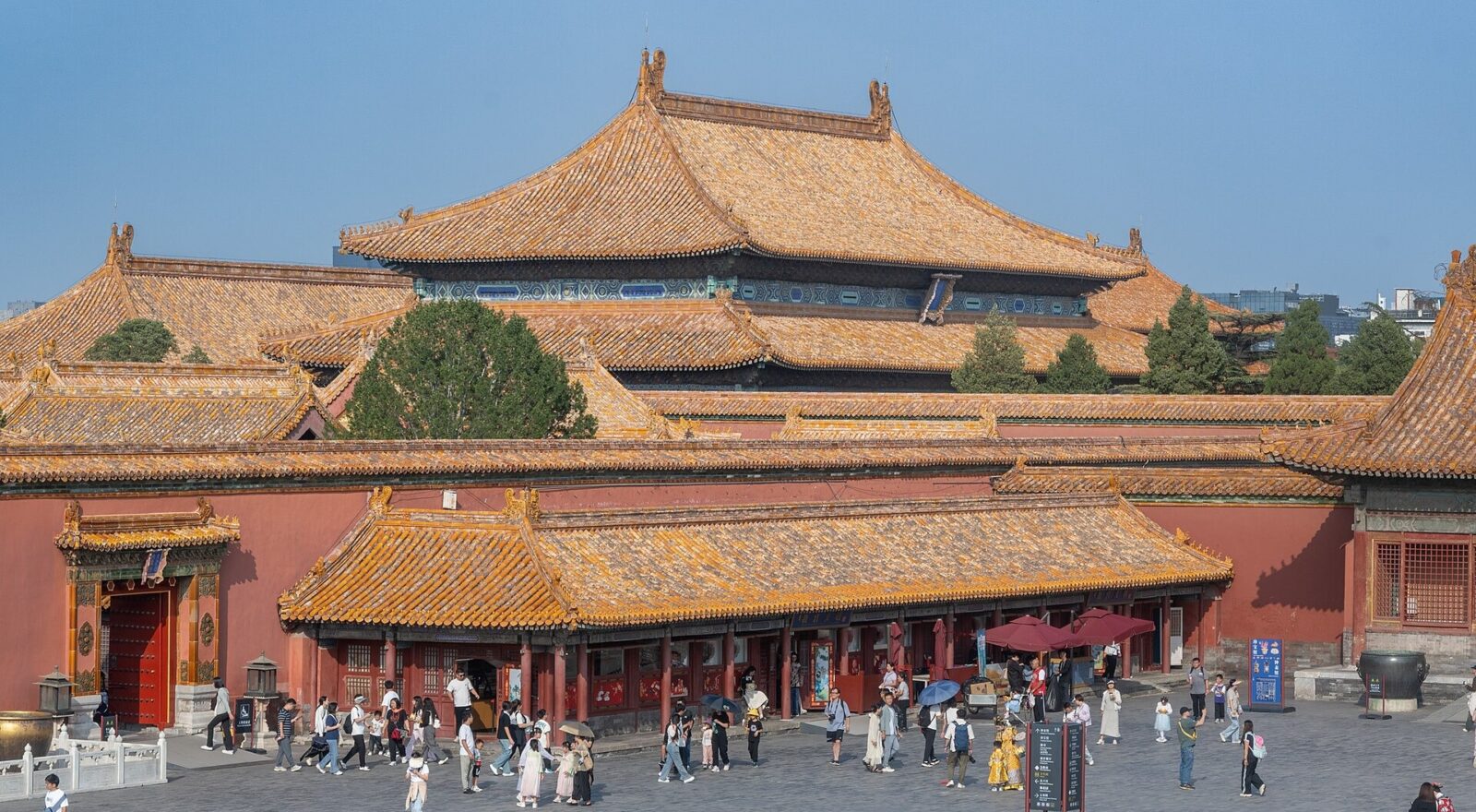 Visitors cross a paved courtyard in Beijing Forbidden City beneath layers of golden tiled palace roofs and red walls.