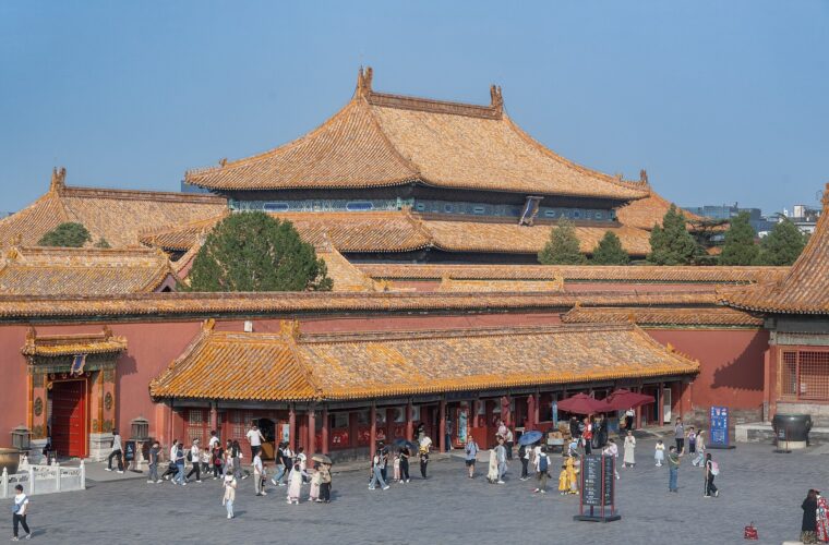Visitors cross a paved courtyard in Beijing Forbidden City beneath layers of golden tiled palace roofs and red walls.