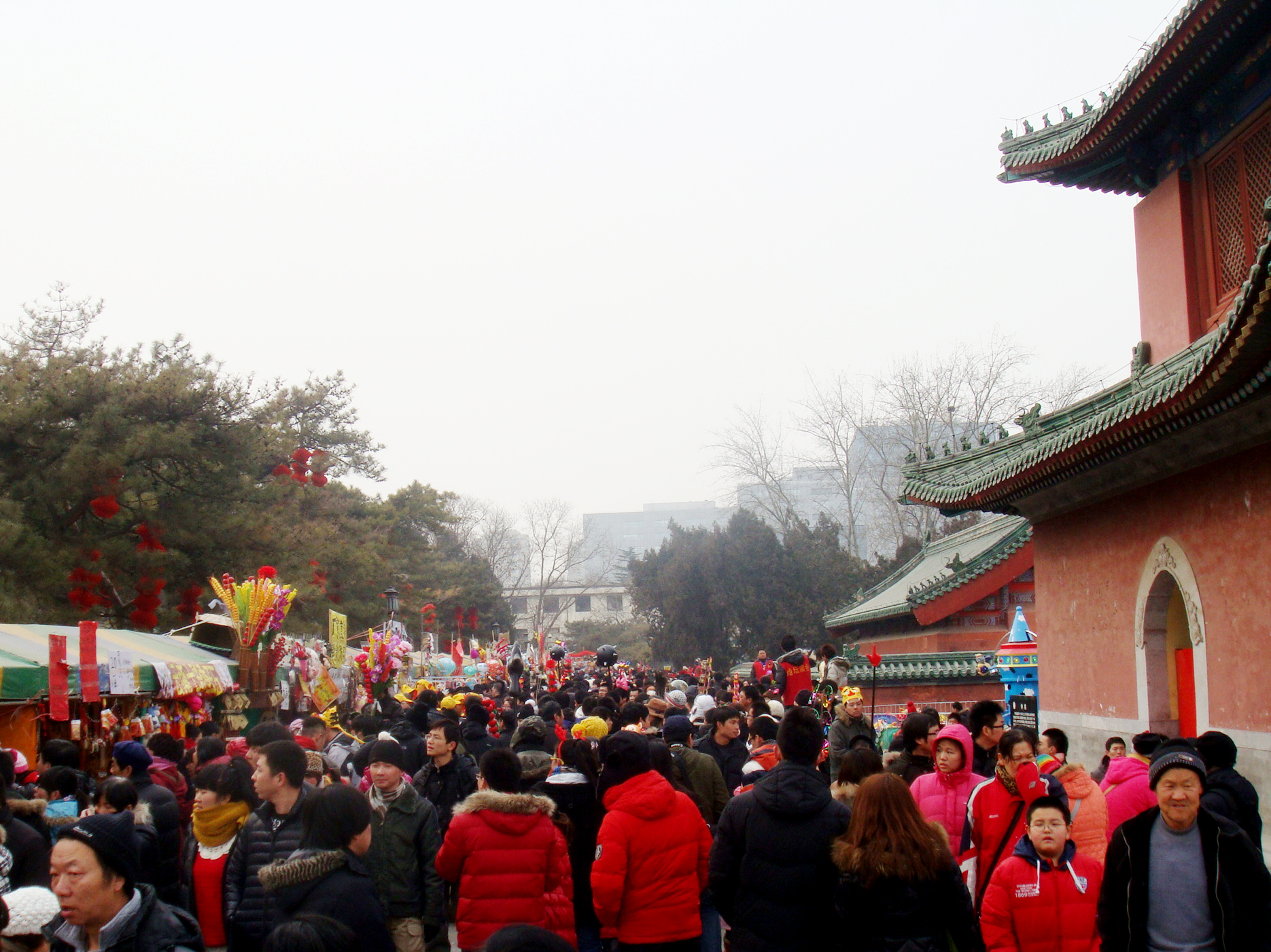 Visitors crowd past colorful toy stalls beside a red gate building at the Ditan temple fair in Beijing.