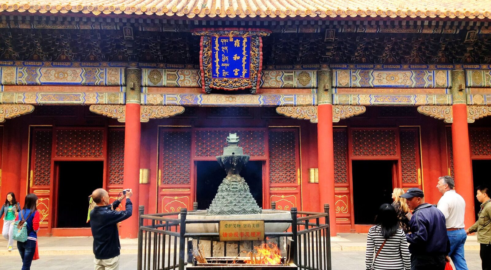 Visitors gather around incense burners beneath the golden tiled roof and painted facade of Yonghe Temple in Beijing.