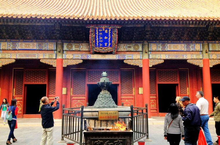 Visitors gather around incense burners beneath the golden tiled roof and painted facade of Yonghe Temple in Beijing.