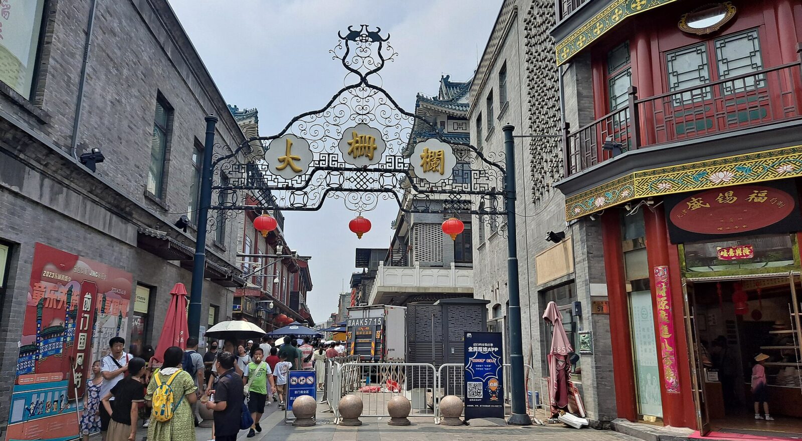 Visitors pass beneath the ornate Dashilar gateway between grey brick walls and a red traditional shopfront in Beijing.