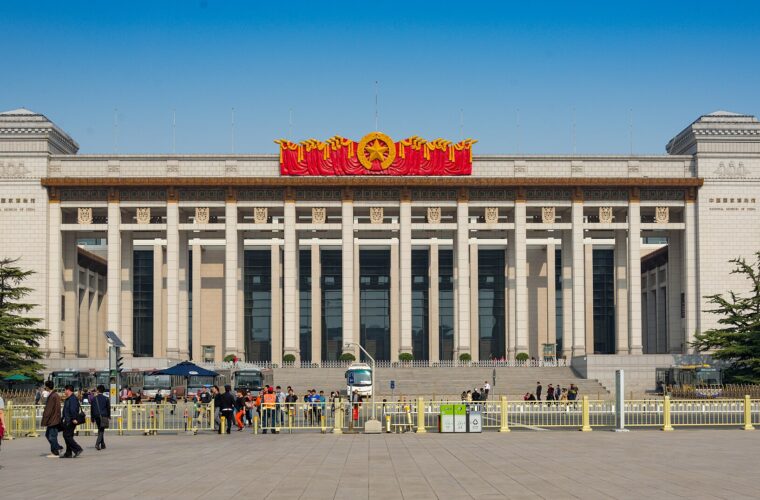 Visitors wait behind barriers outside the columned west entrance of the National Museum of China in Beijing beneath a clear sky.