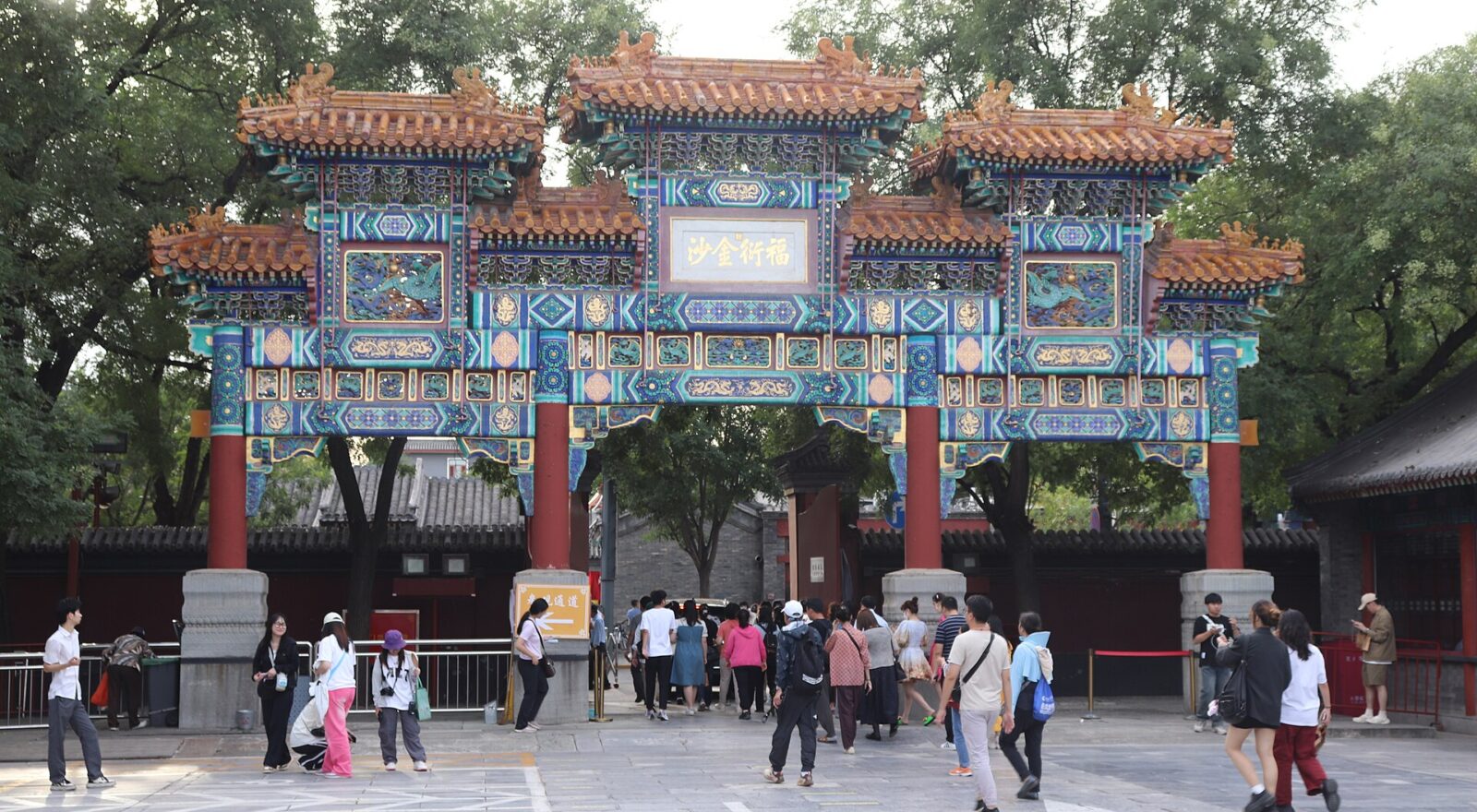 Visitors walk beneath an ornate blue, green and gold archway with red pillars at Beijing's Lama Temple.