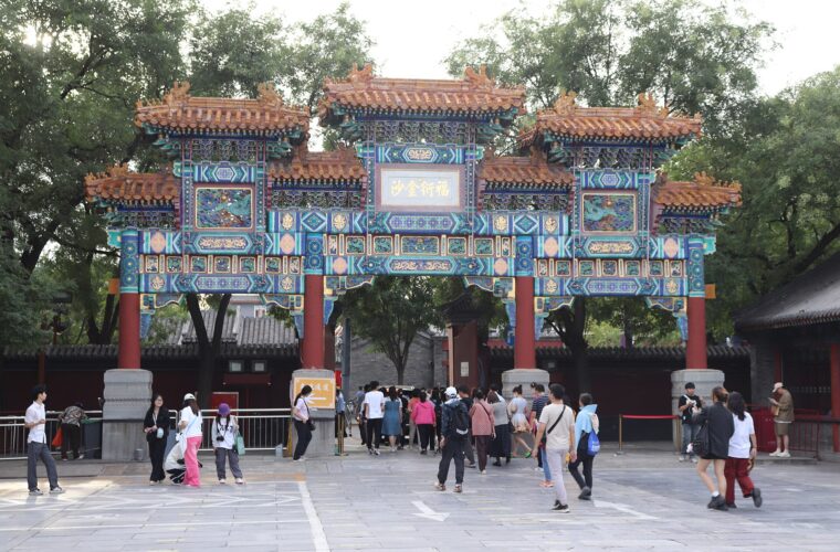 Visitors walk beneath an ornate blue, green and gold archway with red pillars at Beijing's Lama Temple.