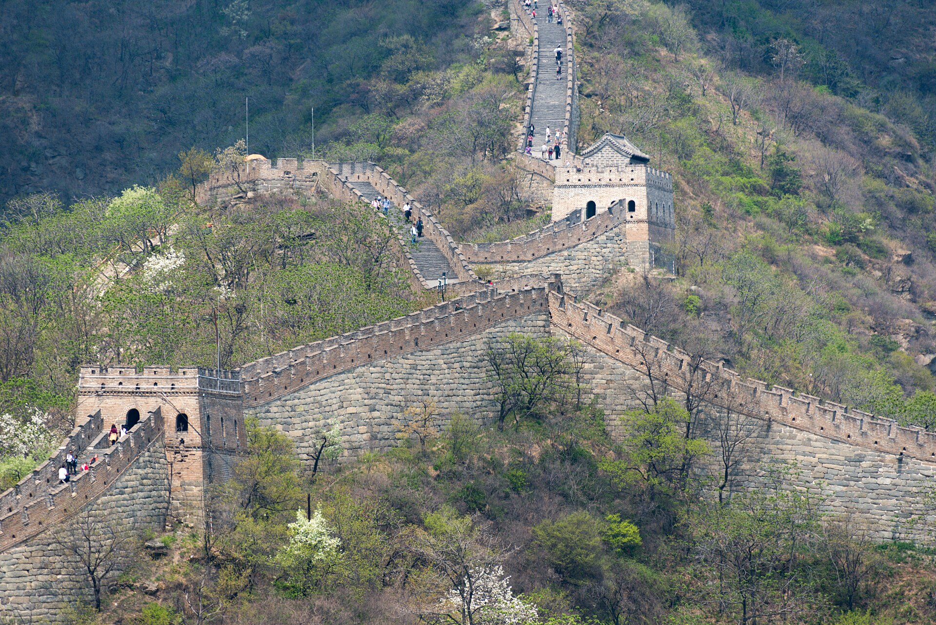 Visitors walk between stone watchtowers on the winding Great Wall at Mutianyu above slopes dotted with spring foliage.